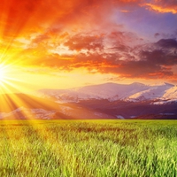 Mountains between grass field and sunset